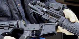 Person assembling a rifle with gloved hands.