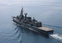 Navy frigate sailing on calm ocean waters.