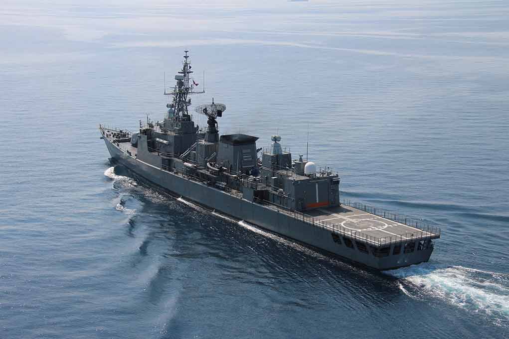 Navy frigate sailing on calm ocean waters.