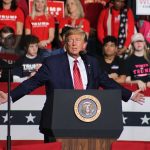 Politician speaking at rally with supporters behind him.