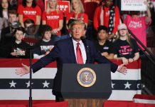 Politician speaking at rally with supporters behind him.