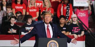 Politician speaking at rally with supporters behind him.