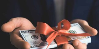 Hands holding stack of hundred-dollar bills with ribbon.