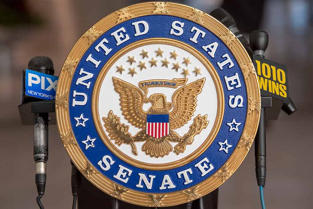 US Senate emblem with microphones in background.