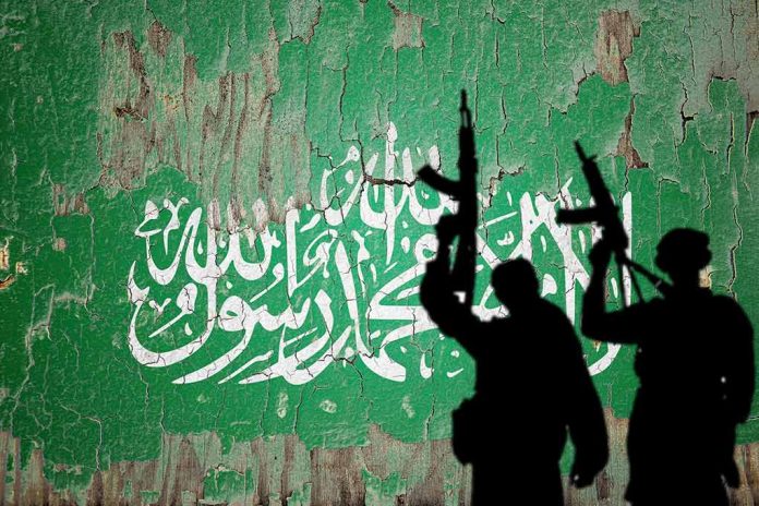 Silhouettes with rifles over Saudi flag background.