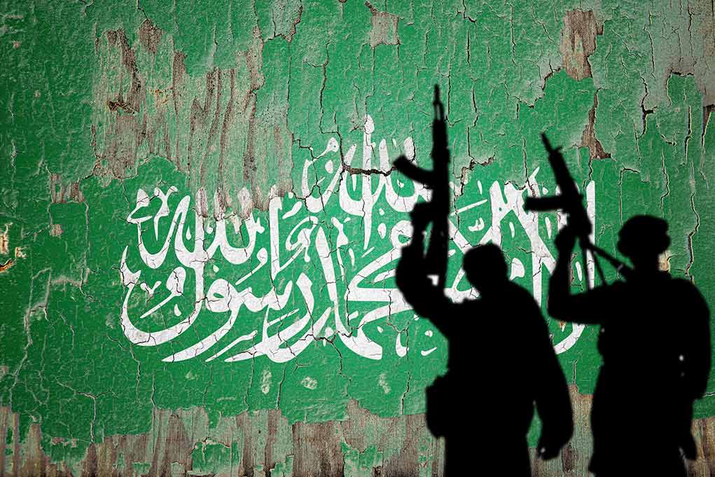 Silhouettes with rifles over Saudi flag background.