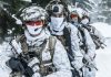 Soldiers in snow camo gear in snowy forest.