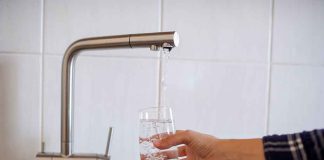 Hand filling glass with water from faucet.