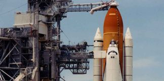 Space shuttle on launch pad with support structure.