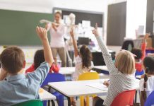 Children raising hands in classroom.