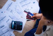 Person holding credit cards amidst bills and calculator