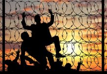 Silhouettes and barbed wire against sunset sky backdrop