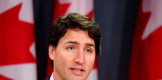 Man speaking in front of Canadian flags.