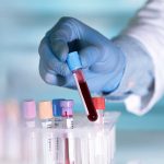 Gloved hand holding a test tube with blood.