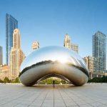 Cloud Gate sculpture with skyline of skyscrapers behind it.