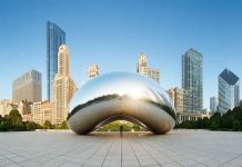 Cloud Gate sculpture with skyline of skyscrapers behind it.