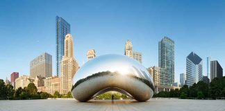 Cloud Gate sculpture with skyline of skyscrapers behind it.