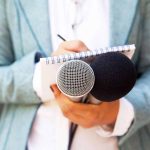 Person holding microphones and a notepad.