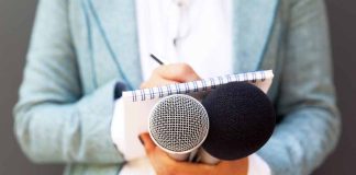 Person holding microphones and a notepad.