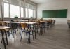 Empty classroom with desks, chairs, windows, and chalkboard.