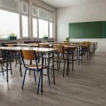 Empty classroom with desks, chairs, windows, and chalkboard.