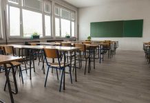 Empty classroom with desks, chairs, windows, and chalkboard.