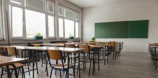 Empty classroom with desks, chairs, windows, and chalkboard.