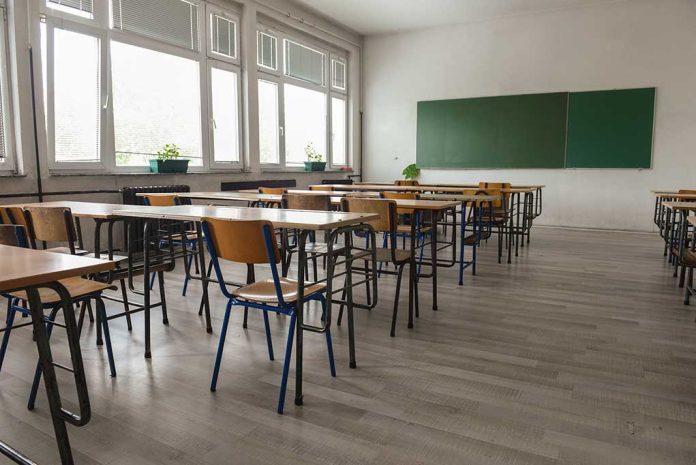 Empty classroom with desks, chairs, windows, and chalkboard.