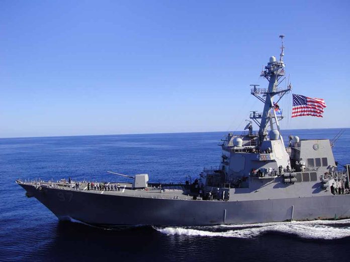 Warship sailing with American flag in open sea.