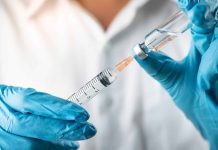 Gloved hands preparing syringe with vaccine vial.