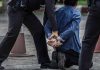 Person kneeling handcuffed by police officers outside