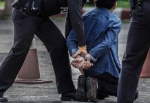 Person kneeling handcuffed by police officers outside