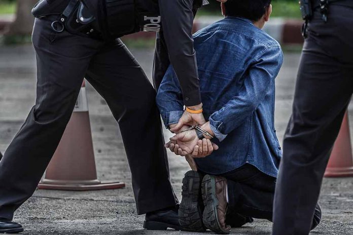 Person kneeling handcuffed by police officers outside